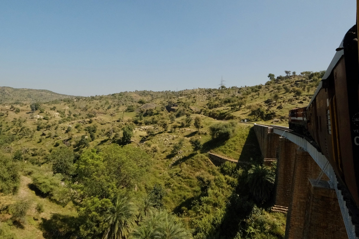 Voyage en train authentique à travers le paysage vert et vallonné du Rajasthan. Idéal pour les voyageurs cherchant un tourisme durable, hors des sentiers battus et des expériences inoubliables en Inde.
